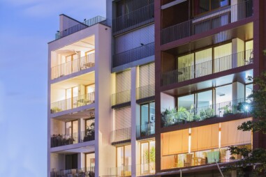 abendlich beleuchtetes modernes Wohnhaus mit Balkonen und großen Fensterflächen
